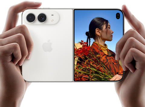 „iPhone Duo“, žvaigždžių balta spalva, laikomas dviem rankomis horizontaliai, išlankstytas; kairėje pusėje matomos 48 MP „Dual Fusion“ galinės kameros, dešinėje išoriniame ekrane rodomas fotografuojamas žmogus, kuris fotografavimo metu mato savo veidą naudodamas „Duo Preview“