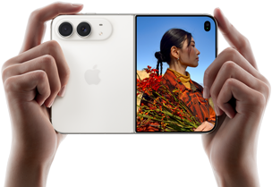 „iPhone Duo“, žvaigždžių balta spalva, laikomas dviem rankomis horizontaliai, išlankstytas; kairėje pusėje matomos 48 MP „Dual Fusion“ galinės kameros, dešinėje išoriniame ekrane rodomas fotografuojamas žmogus, kuris fotografavimo metu mato savo veidą naudodamas „Duo Preview“