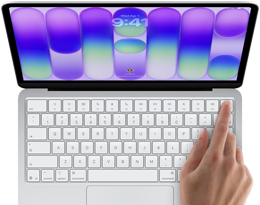 MacBook Neo, sidabrinės spalvos, rodomas prisijungimo ekranas, žmogaus pirštas liečia Touch ID jutiklį viršutiniame dešiniajame klaviatūros kampe